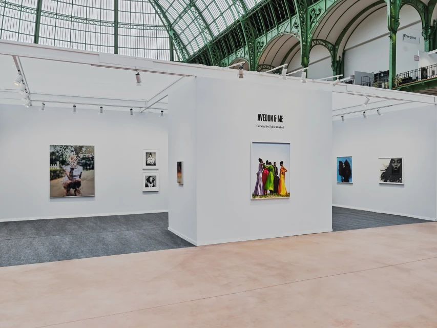 Interior view of a photo exhibition with colorful photos displayed on white walls under an elaborate glass and steel roof structure.
