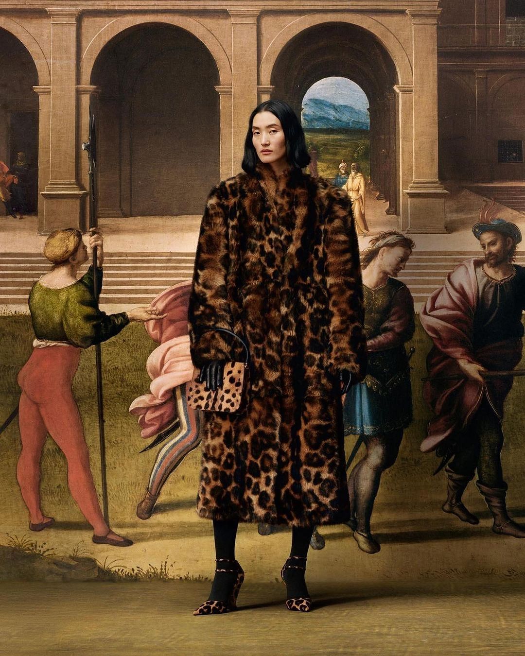 A woman poses in a leopard-print coat against a Renaissance-style mural, blending modern fashion with classic art aesthetics.