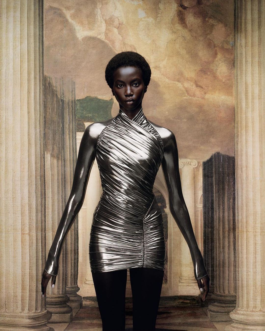 A striking image features a singular Black female fashion model in a metallic dress, confidently posed against a classical backdrop.