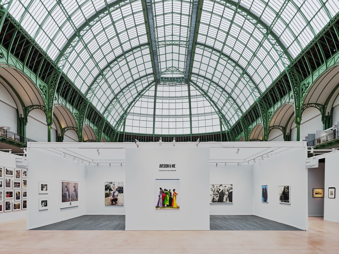 Interior view of an art exhibition featuring photograph displays within a hall with a large arched, green-framed glass ceiling.