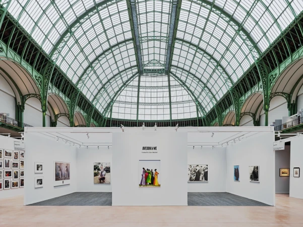 Interior view of an art exhibition featuring photograph displays within a hall with a large arched, green-framed glass ceiling.