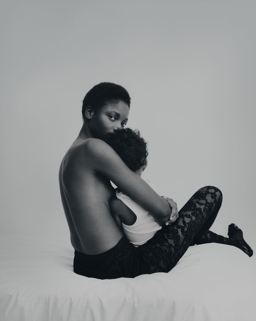 A mother gently embraces her child in a monochrome studio portrait, showcasing a tender moment of connection and familial love.