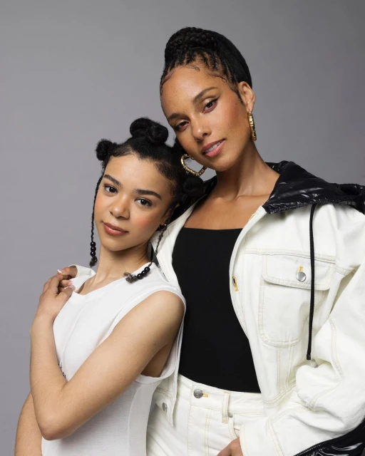 Headshot of singer Alicia Keys with a young woman, both posing closely with a gray background. Alicia Keys wears a black top and white jacket.