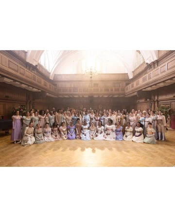 Large group of people gathered indoors on a wooden floor with elegant architecture. People are in dresses and formal wear.