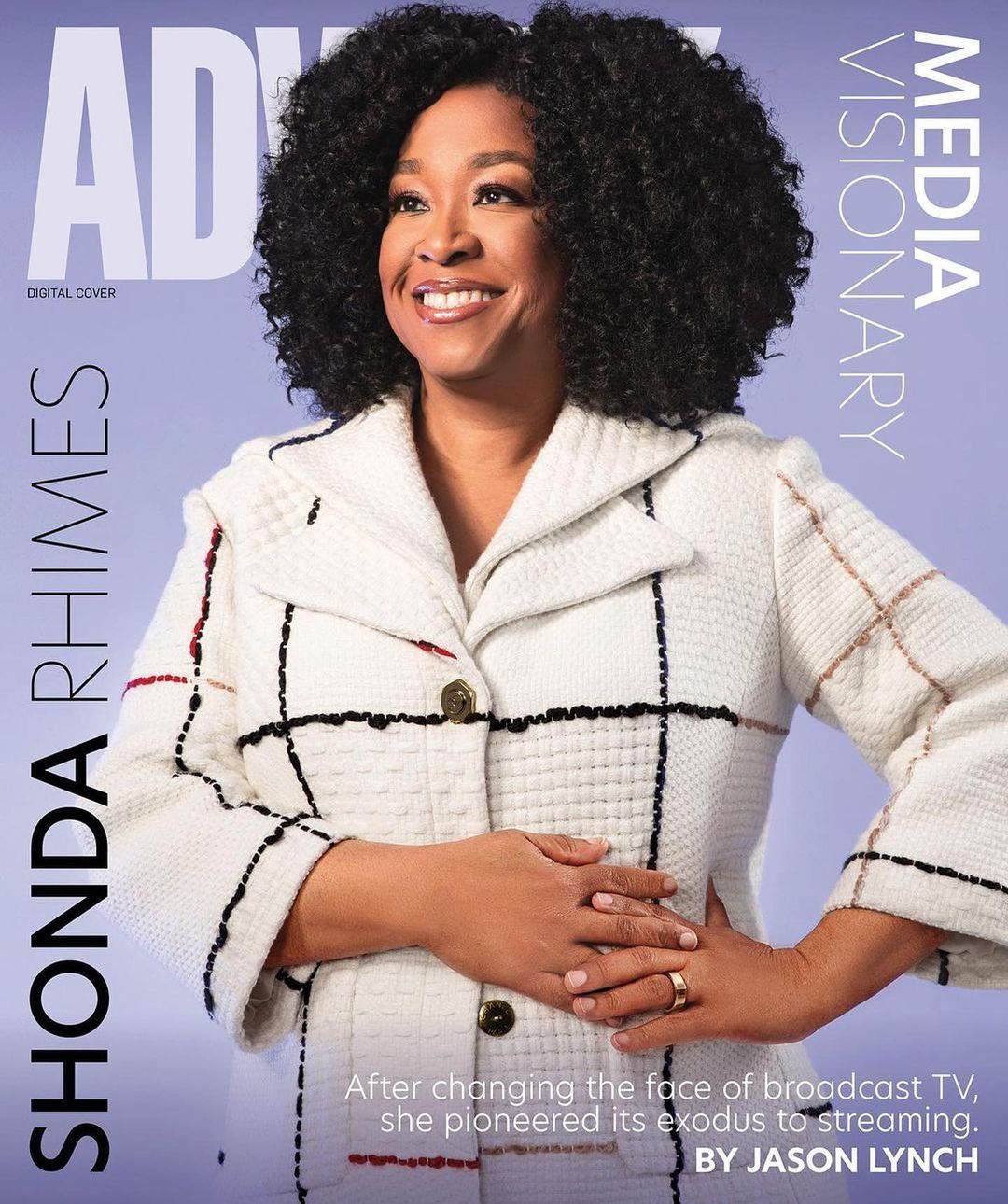 Shonda Rhimes smiles on a magazine cover, wearing a patterned white coat against a light purple backdrop with visible magazine text.