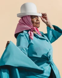 Elderly woman wearing a teal coat, pink headscarf, and white bowler hat photographed by Tyler Twins.