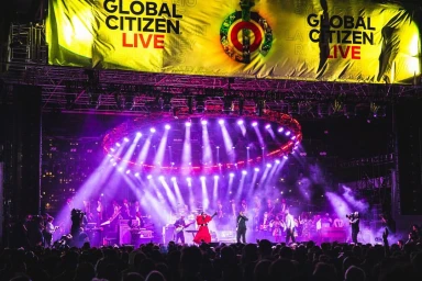Concert stage with vibrant purple lighting overhead, a band performing, and a large Global Citizen Live banner above.