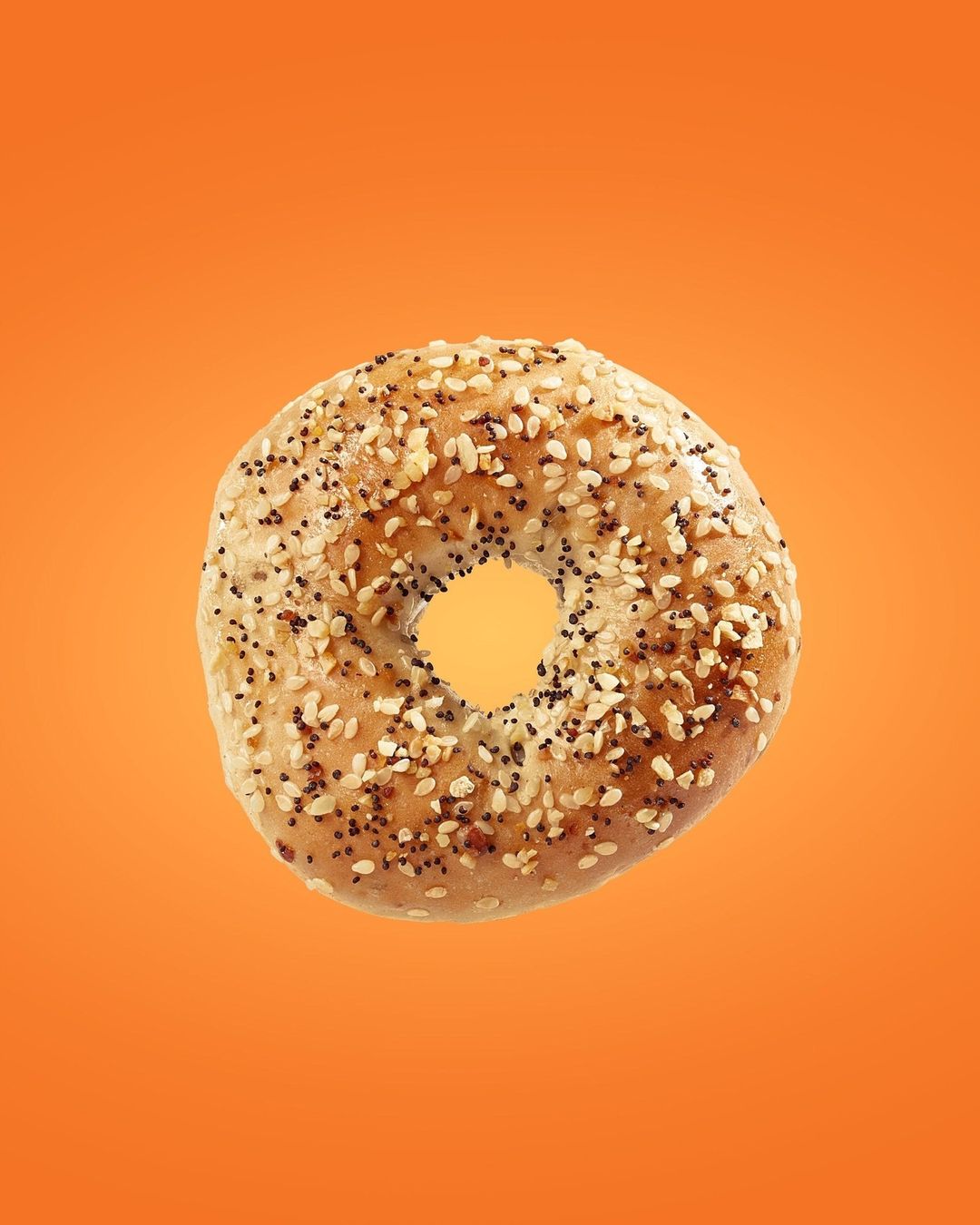 A sesame-covered bagel is centered against a bright orange background, emphasizing its round shape and textured surface. 