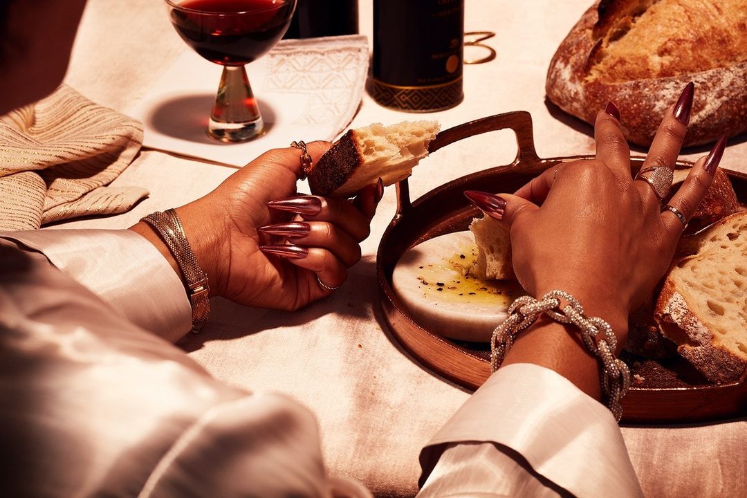Close-up of a person's hands breaking bread at a dinner table set with wine and marble board with olive oil.