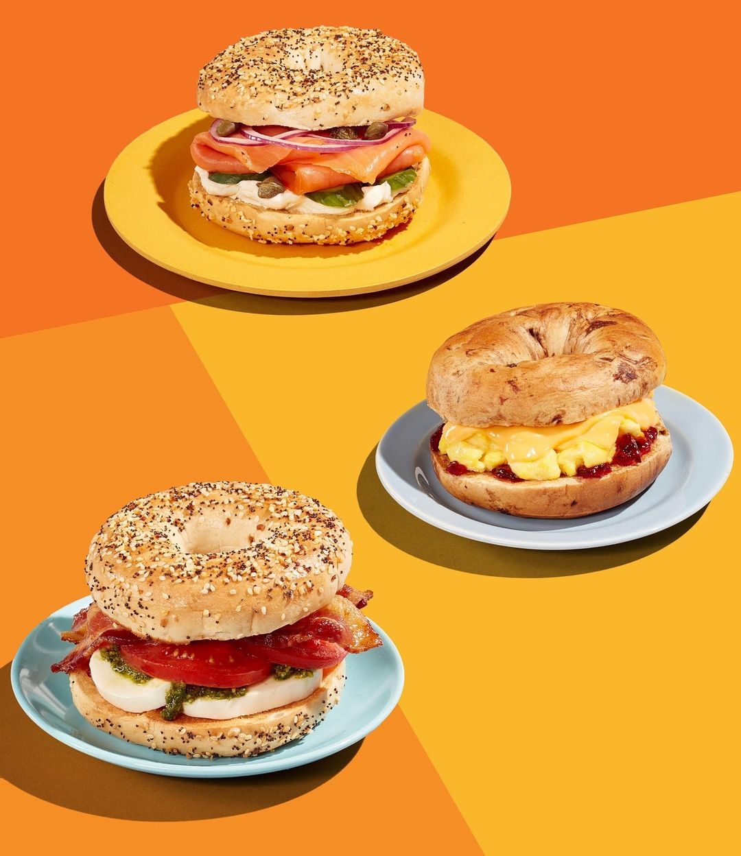 Three bagel sandwiches with different toppings arranged on yellow, orange, and blue plates against a split yellow and orange background.