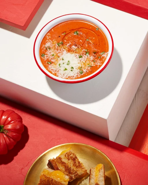 Overhead view of tomato soup with grilled cheese sandwiches on a red and white table, creating a warm and inviting food photography image.