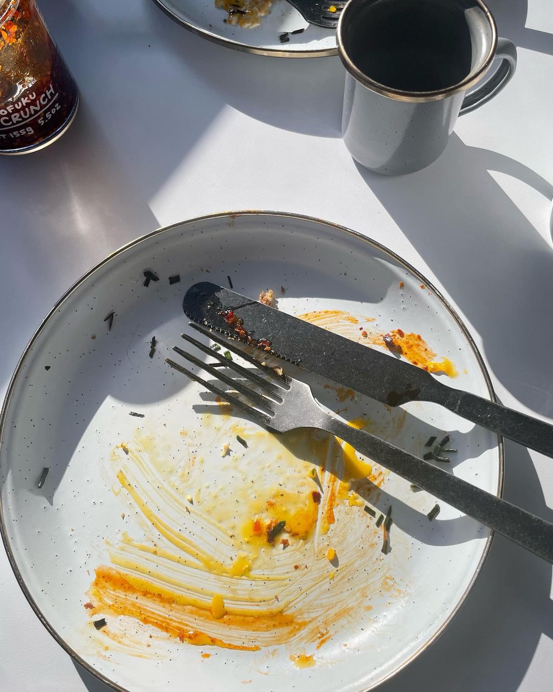 Overhead shot of a mostly empty plate with a fork, knife, and food remnants on a white table, and a glass and mug on the side.