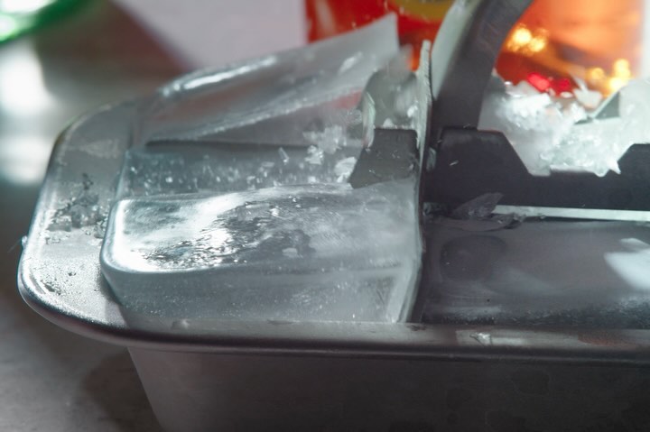 Close-up of an ice cube tray partially filled with water and broken ice, showcasing textures and reflections on the icy surface.