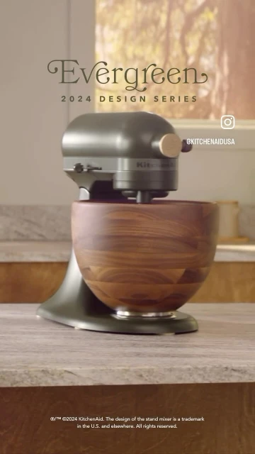 Olive green KitchenAid stand mixer with wooden bowl on counter in bright kitchen. Evergreen 2024 Design Series promotion.