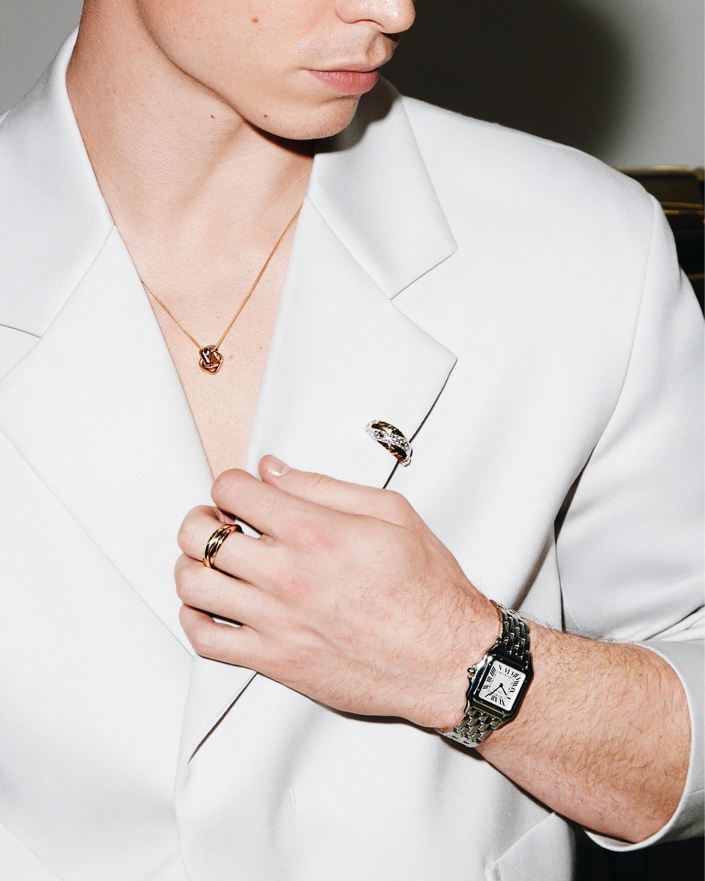 Close-up of a stylish adult male wearing a white blazer, gold jewelry, and a watch, highlighting fashion and accessorizing.