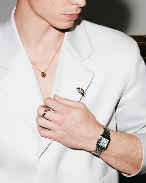 Close-up of a stylish adult male wearing a white blazer, gold jewelry, and a watch, highlighting fashion and accessorizing.