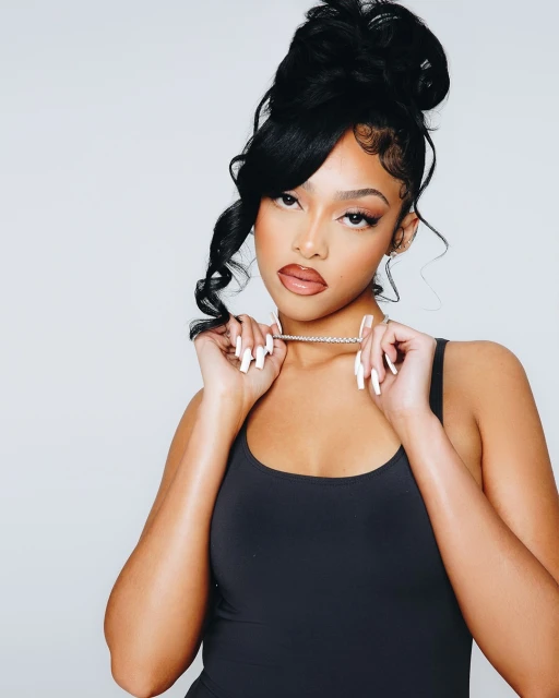 Elegant woman with high updo and black top wearing a necklace poses in a brightly lit studio setting with a neutral background.