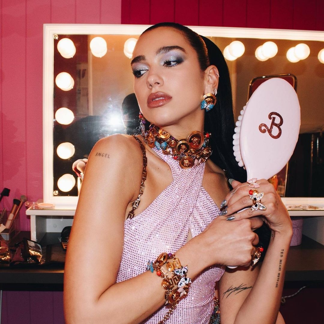 Woman in pink dress wearing jewelry poses in front of lighted mirror. Beauty shot of model in makeup with ornate collar and bracelets.