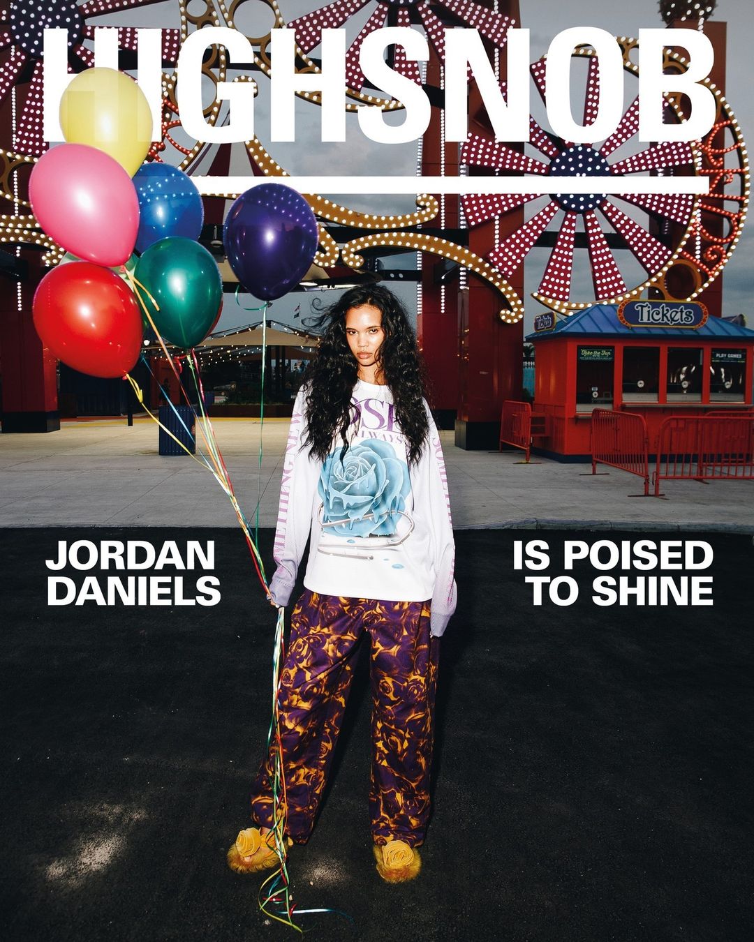 Young woman poses with balloons in front of a Ferris wheel for a Highsnobriety magazine cover in an outdoor urban environment.