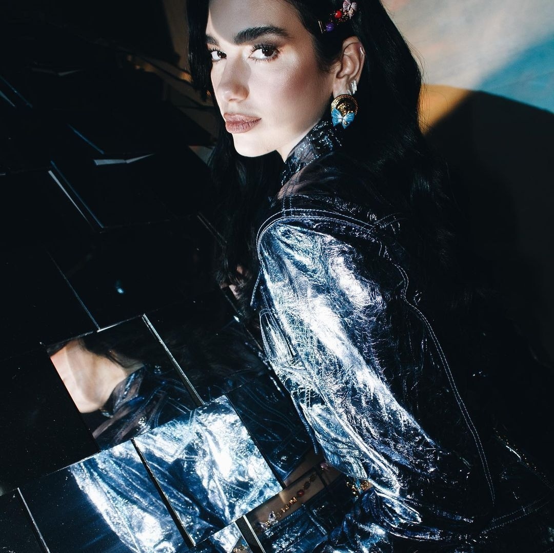 Portrait of a young woman in a shiny jacket. She is adorned with decorative hair clips and earrings while posing indoors.