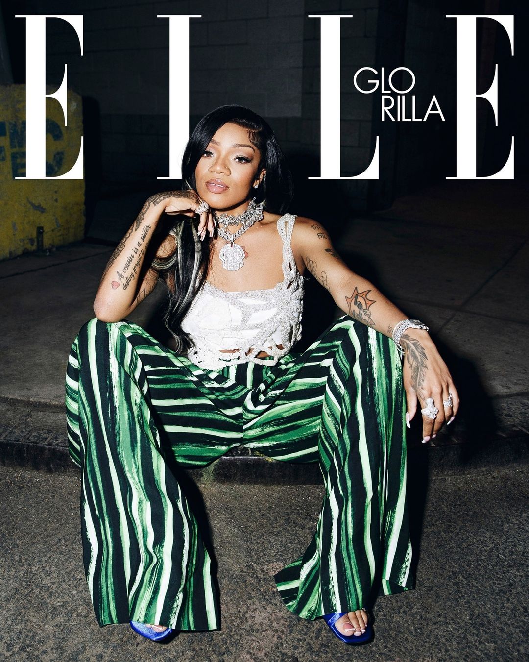 Elle magazine cover featuring GloRilla sitting on concrete, wearing a white top, wide-leg striped pants, jewelry, and blue high heels.