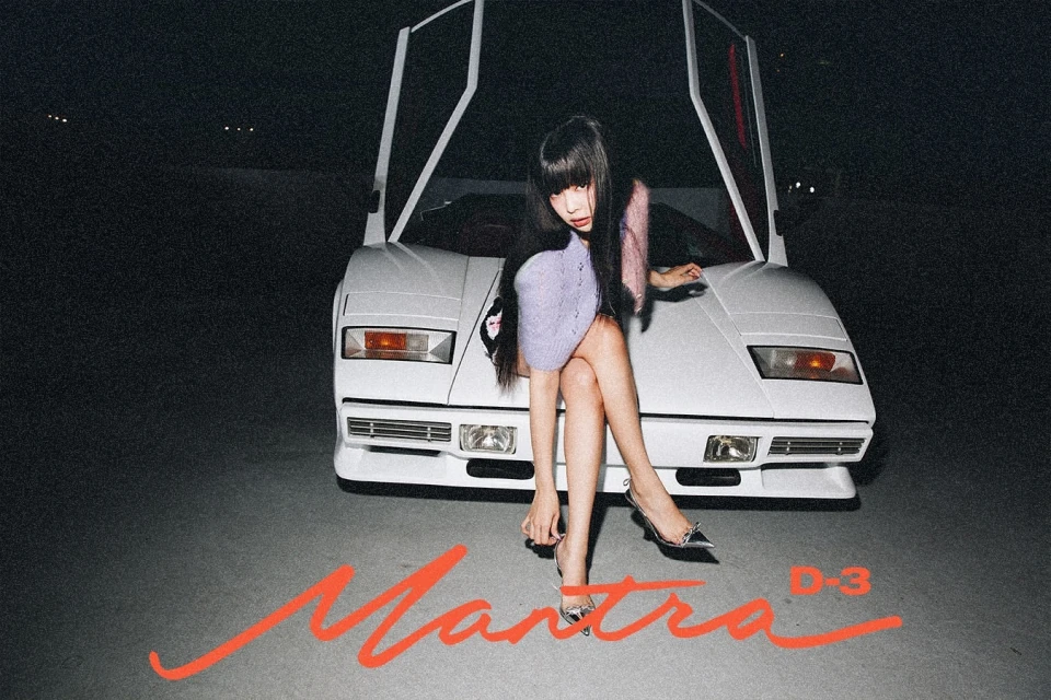 Young woman poses in front of a vintage white sports car at night, wearing a lavender dress and silver heels. Studio shot.