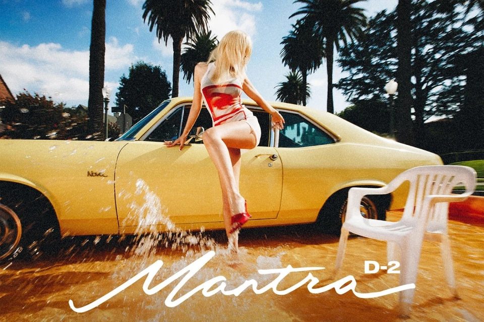 Adult woman strikes a pose on a yellow classic car with a white chair near a flooded street under a blue sky with palm trees.