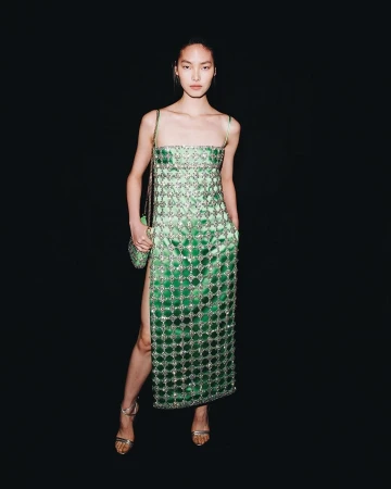 An Asian fashion model poses in a green sequin dress and strappy heels with a sequined purse against a plain black background.