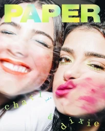 Close-up portrait of two smiling young women posing together with bright makeup and pink lipstick smudged on one cheek.