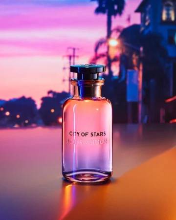 A perfume bottle stands on a reflective surface against a vibrant purple and pink sunset sky with silhouettes of palm trees.