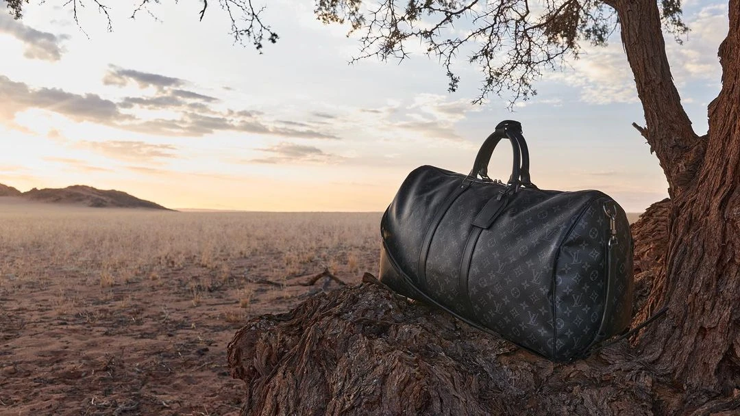 Leather duffel bag sits near a tree in a savanna landscape. The light of the setting sun glows over dry grass and distant hills.