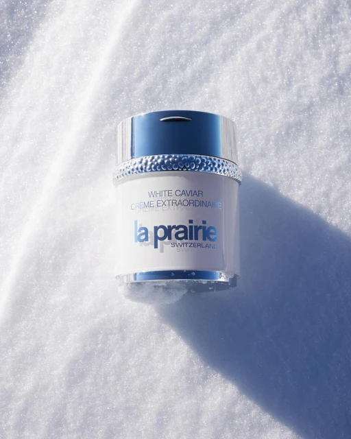La Prairie White Caviar Crème Extraordinaire jar on white, glittering snow background with a silver lid and blue logo.