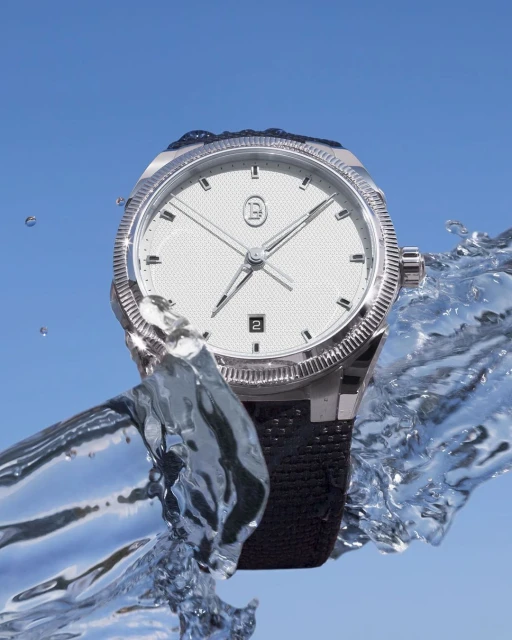 Silver wristwatch with a white face and black band is presented against a backdrop of flowing water and a light blue sky.