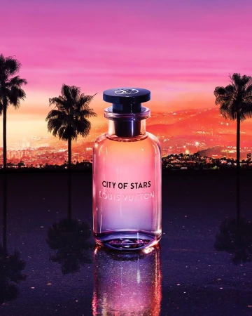 Louis Vuitton 'City of Stars' perfume bottle on a reflective surface, featuring palm trees, city lights, and a vibrant sunset backdrop.