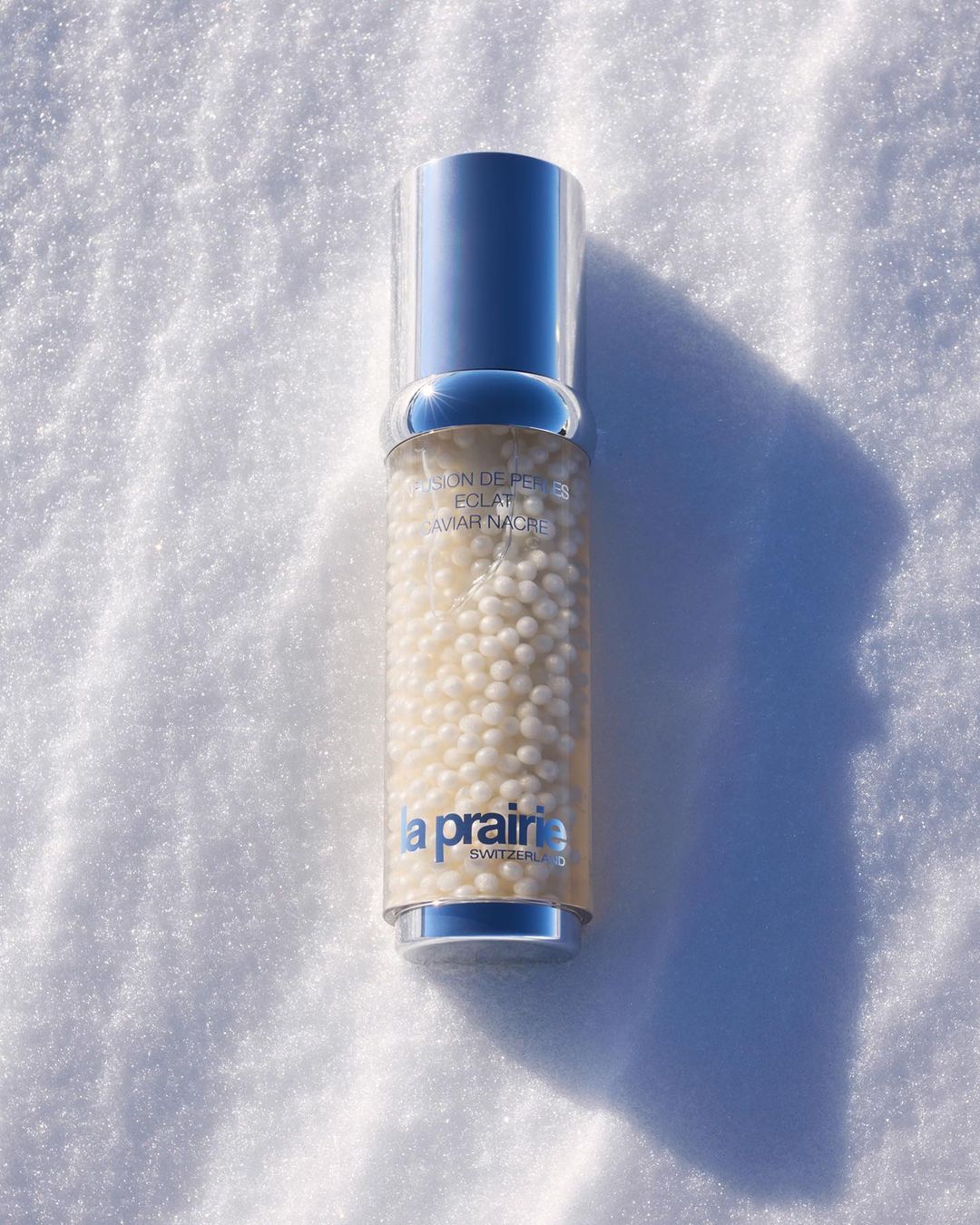 La Prairie skincare bottle filled with small white pearls on snow, silver cap. Beauty and skincare product in natural outdoor setting.