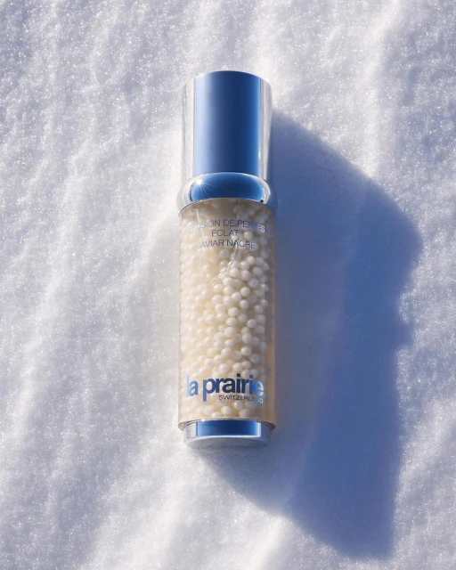 La Prairie skincare bottle filled with small white pearls on snow, silver cap. Beauty and skincare product in natural outdoor setting.
