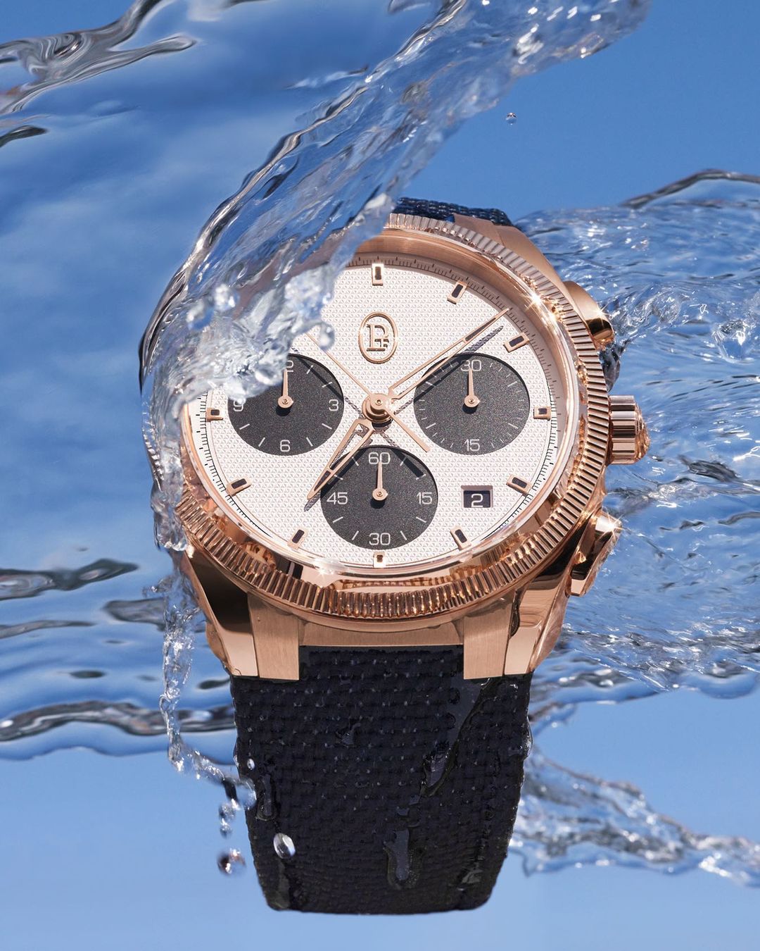 Luxury gold wristwatch with a black band displayed with a water splash, showcasing details against a clear blue background.