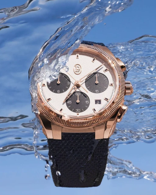 Luxury gold wristwatch with a black band displayed with a water splash, showcasing details against a clear blue background.