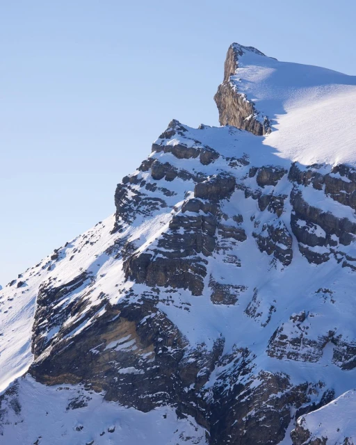Scenic view of a snow-covered mountain peak with rock formations against a clear blue sky, perfect for travel and nature photography.
