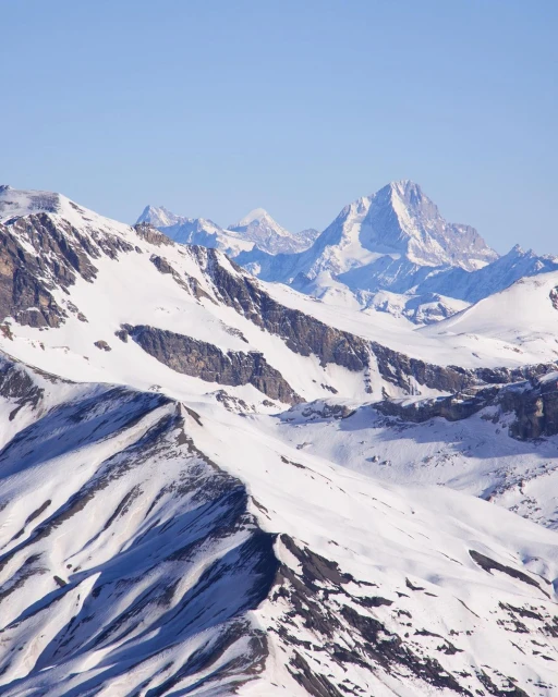 Snowy mountain range landscape under a clear blue sky. White snow covers the mountain peaks and slopes in the distance.