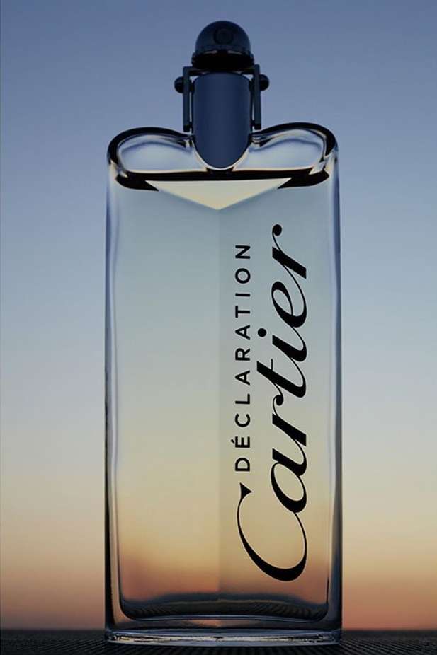 Crystal perfume bottle with Cartier Déclaration branding against a gradiated blue and yellow sky evoking luxury and modern design.