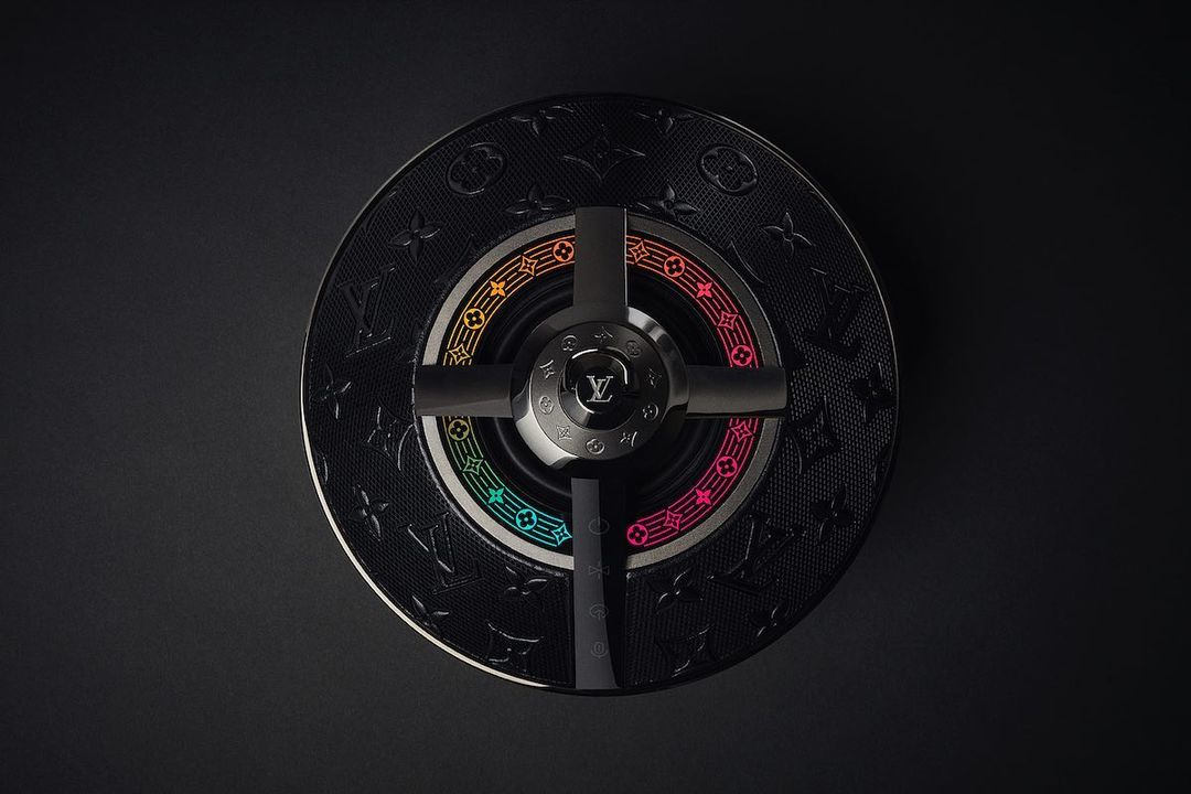 Overhead studio shot of a black Louis Vuitton ashtray with a rainbow-colored ring and four black supports on a dark gray background.