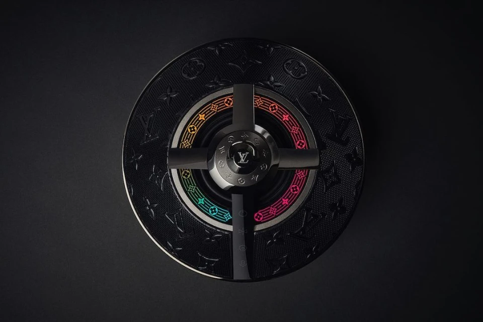 Overhead studio shot of a black Louis Vuitton ashtray with a rainbow-colored ring and four black supports on a dark gray background.