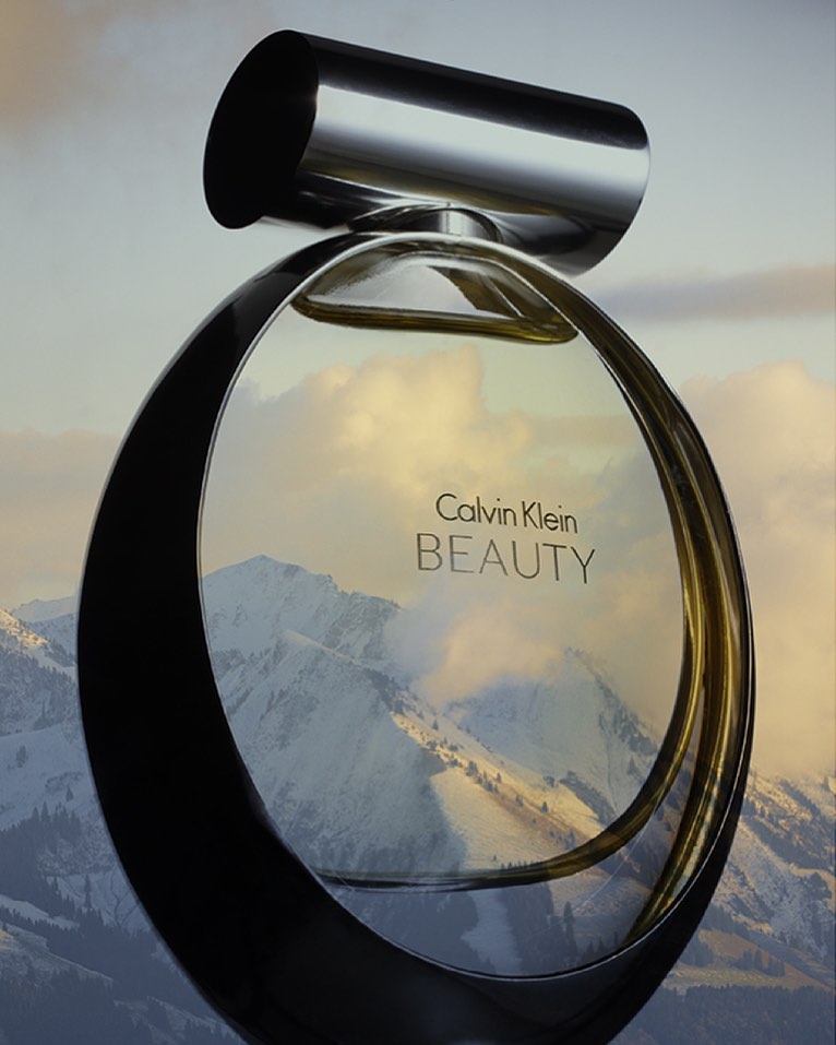 Calvin Klein Beauty perfume bottle in front of snow-covered mountains and cloudy sky, showcasing product and natural beauty backdrop.