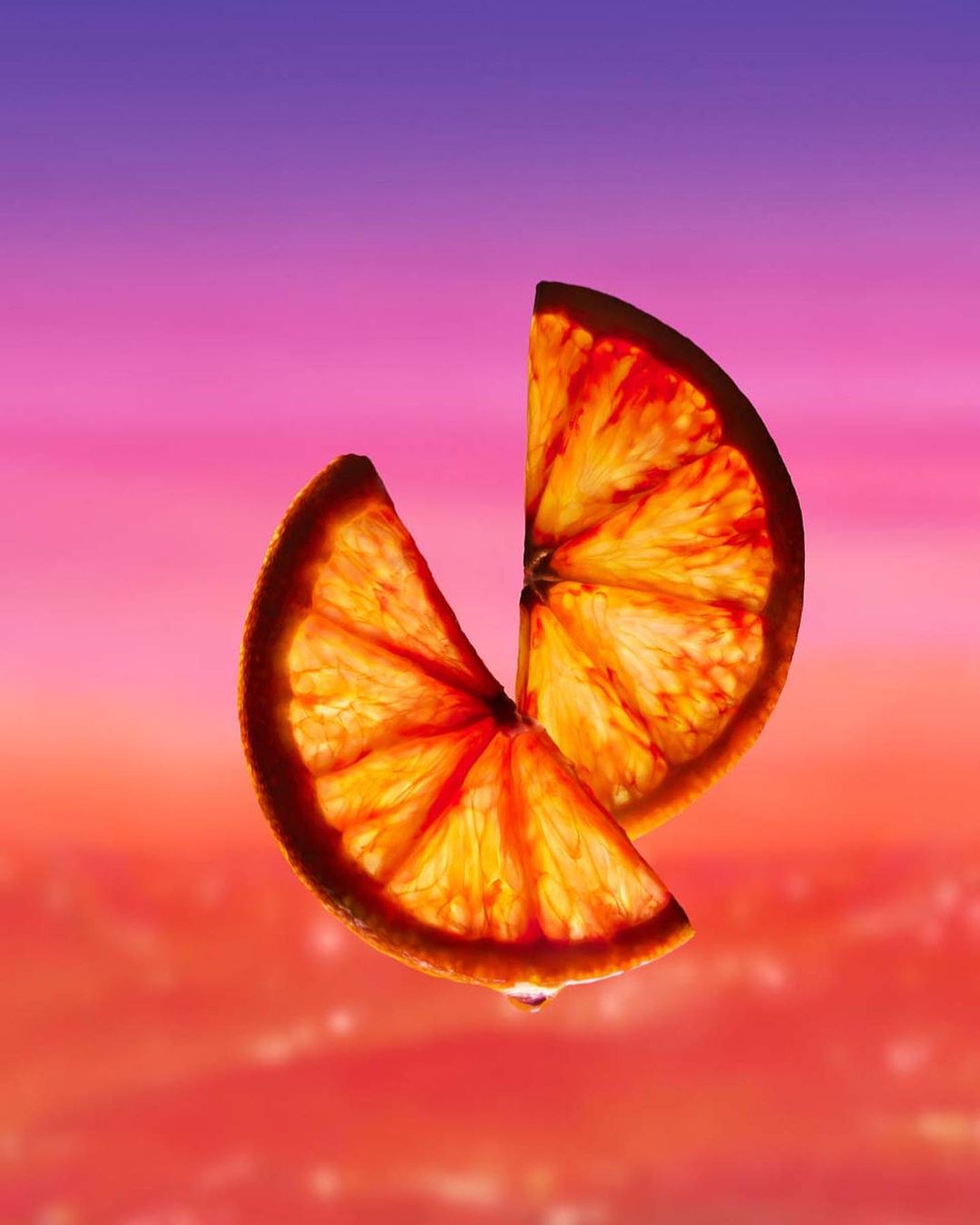 Two orange segments, stacked, and backlit against a blurred pink and orange background, highlighting vibrant colors and citrus texture.