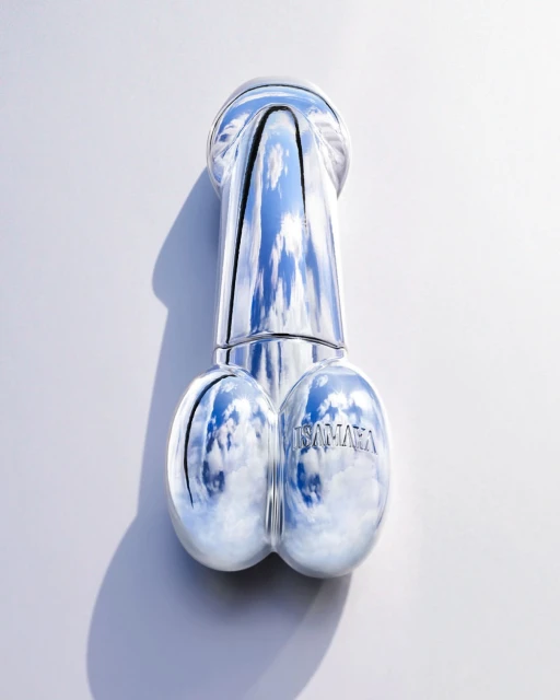 Shiny silver sculpture on a white surface reflecting a blue sky with clouds, creating a surreal and eye-catching abstract artwork.