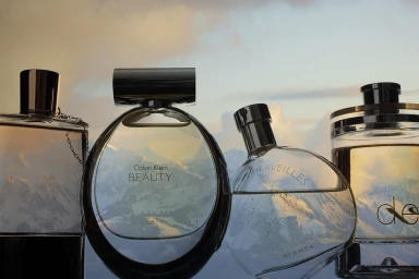 Four perfume bottles standing in a row against a mountain landscape background with a cloudy sky at sunset.