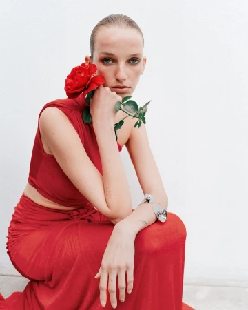 Woman in red dress poses with red rose against a white background in a fashion-style portrait with a neutral expression.