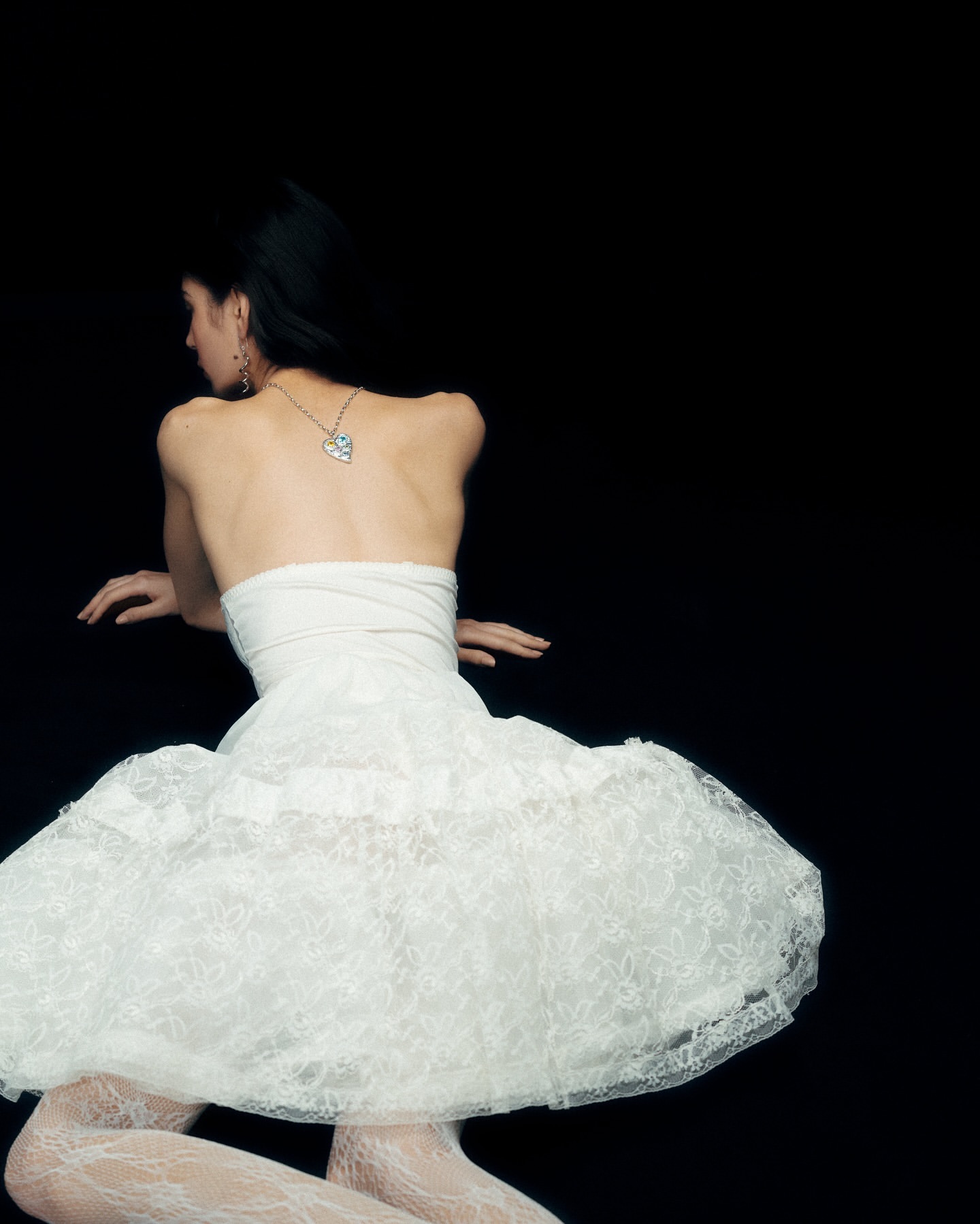Woman in white dress and lace tights poses against a black backdrop, showcasing fashion and elegance, with a shallow depth of field.