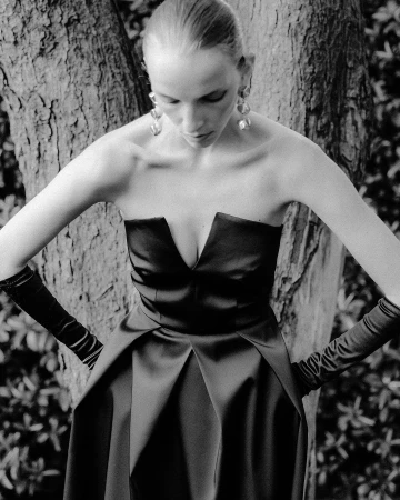 Monochrome portrait of a model in a strapless black dress and long gloves posing against a textured tree trunk